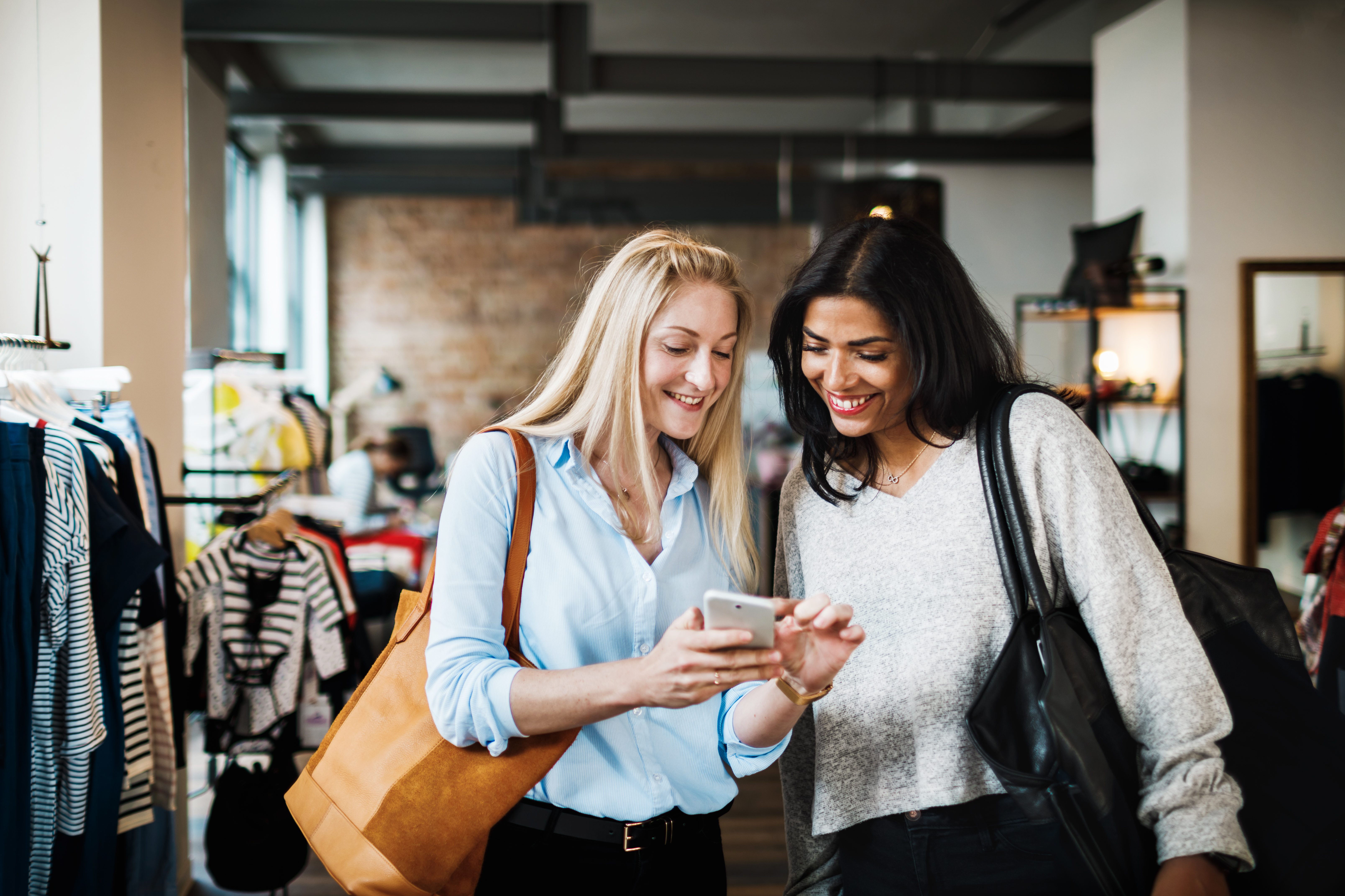 Two women standing in a store, smiling and looking at a mobile phone