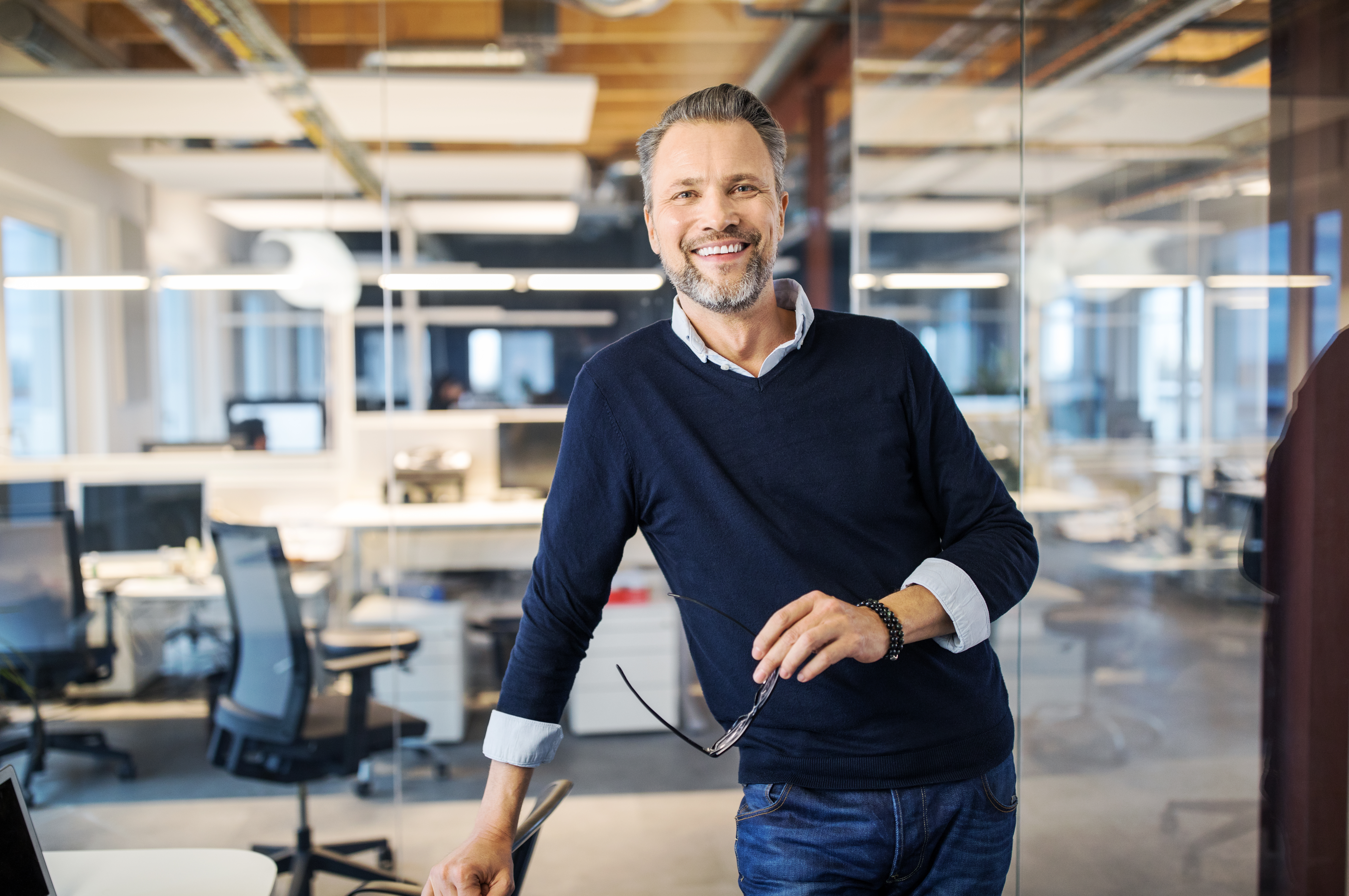 Man standing in office, smiling towards the camera and holding glasses