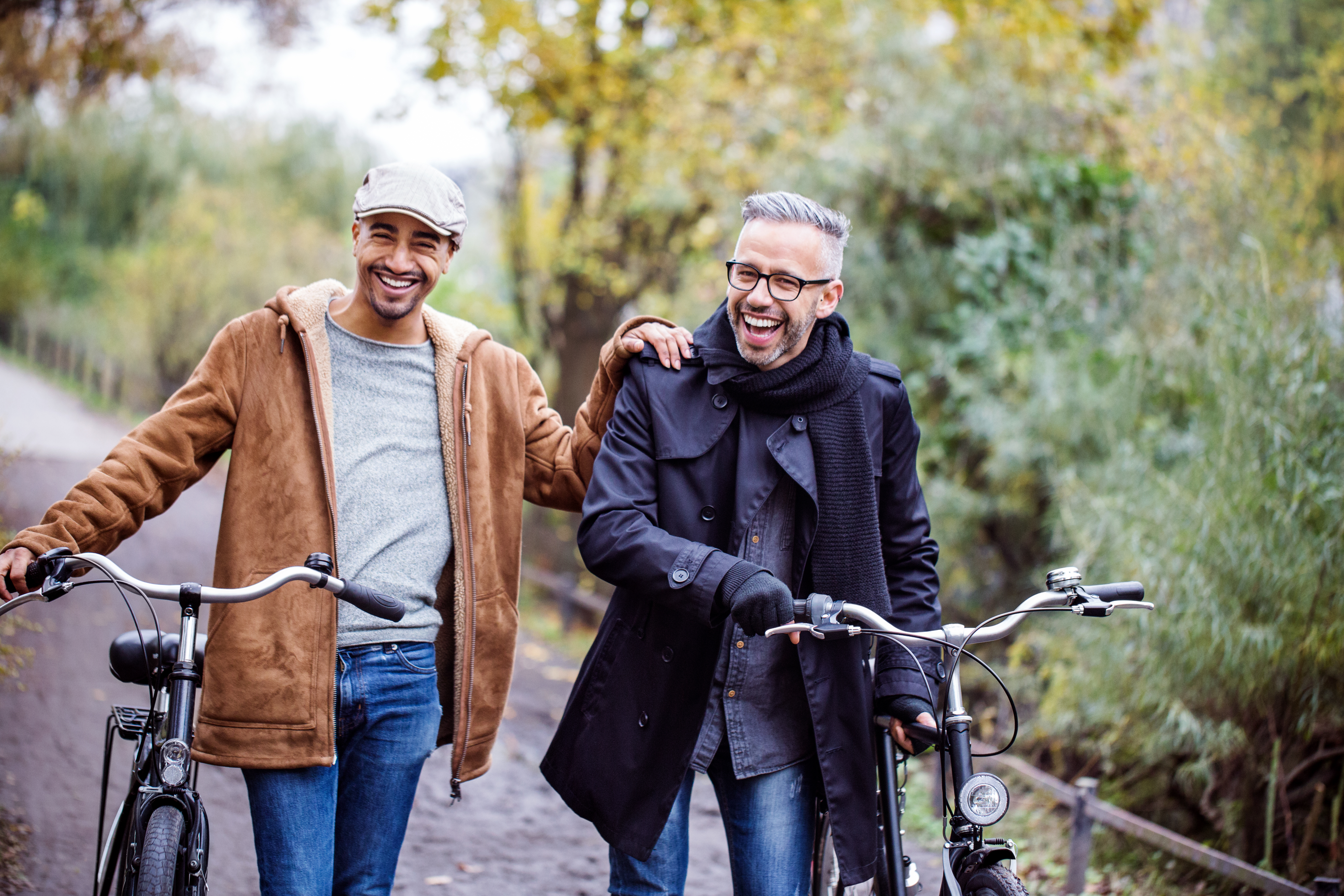 Two laughing men walking with their bicycles